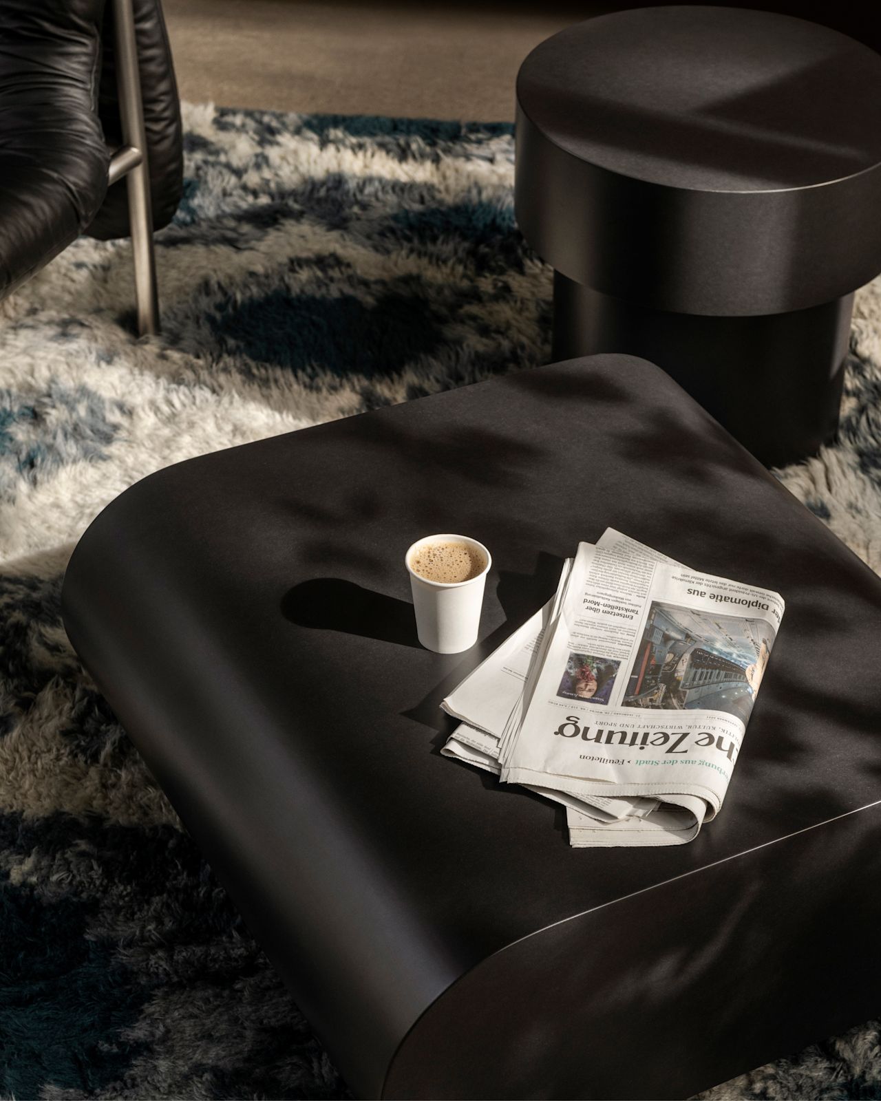 A lifestyle image of a lounge scene featuring Stump Coffee Table Medium Black, Stump Side Table Black, and Monster Rug.