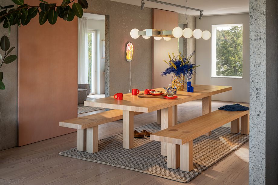 A lifestyle image of a dining scene featuring Knuckle Linear Chandelier, Bronto Tableware, Max Table + Benches Set, Rope Rug, Brute Vase, and Globos Neon.