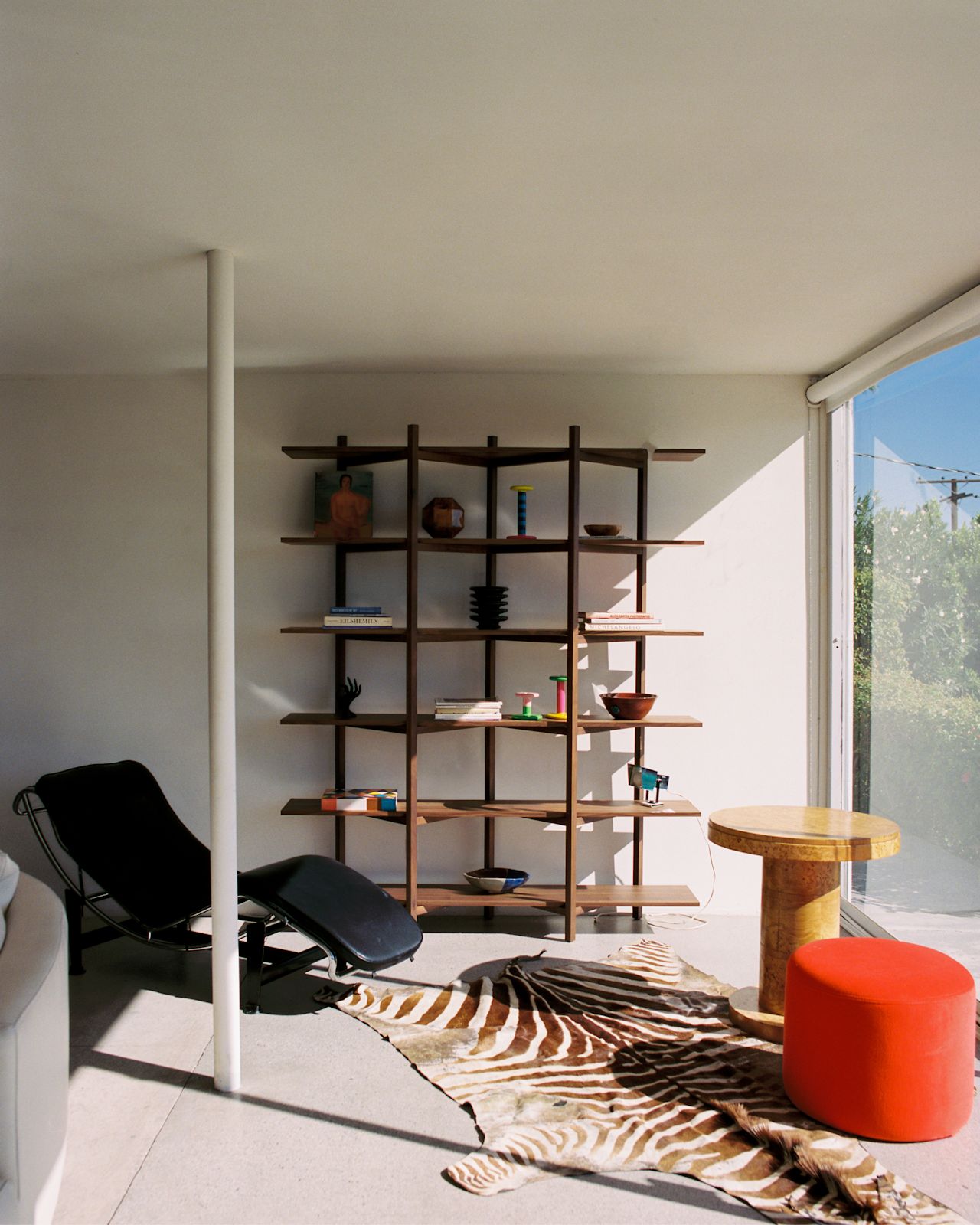 A lifestyle image of a lounge scene featuring Pesa Candle Holder, Zig Zag High Shelf Walnut, and Bon Pouf Round Red.