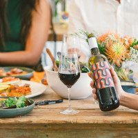 Person holding a bottle of wine at a table with friends