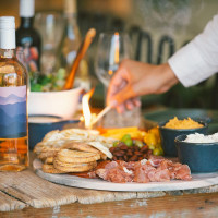 Charcuterie board on a rustic wooden table, with a bottle of Postino Altura wine next to it