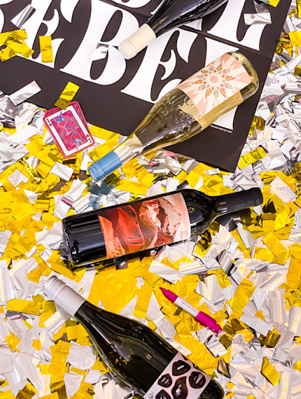 Four Bottles of Wine laying on a gold and silver celebratory confetti backdrop.
