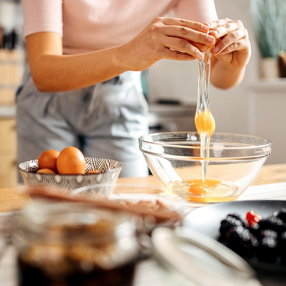 Une femme casse des œufs dans une casserole - Aveve