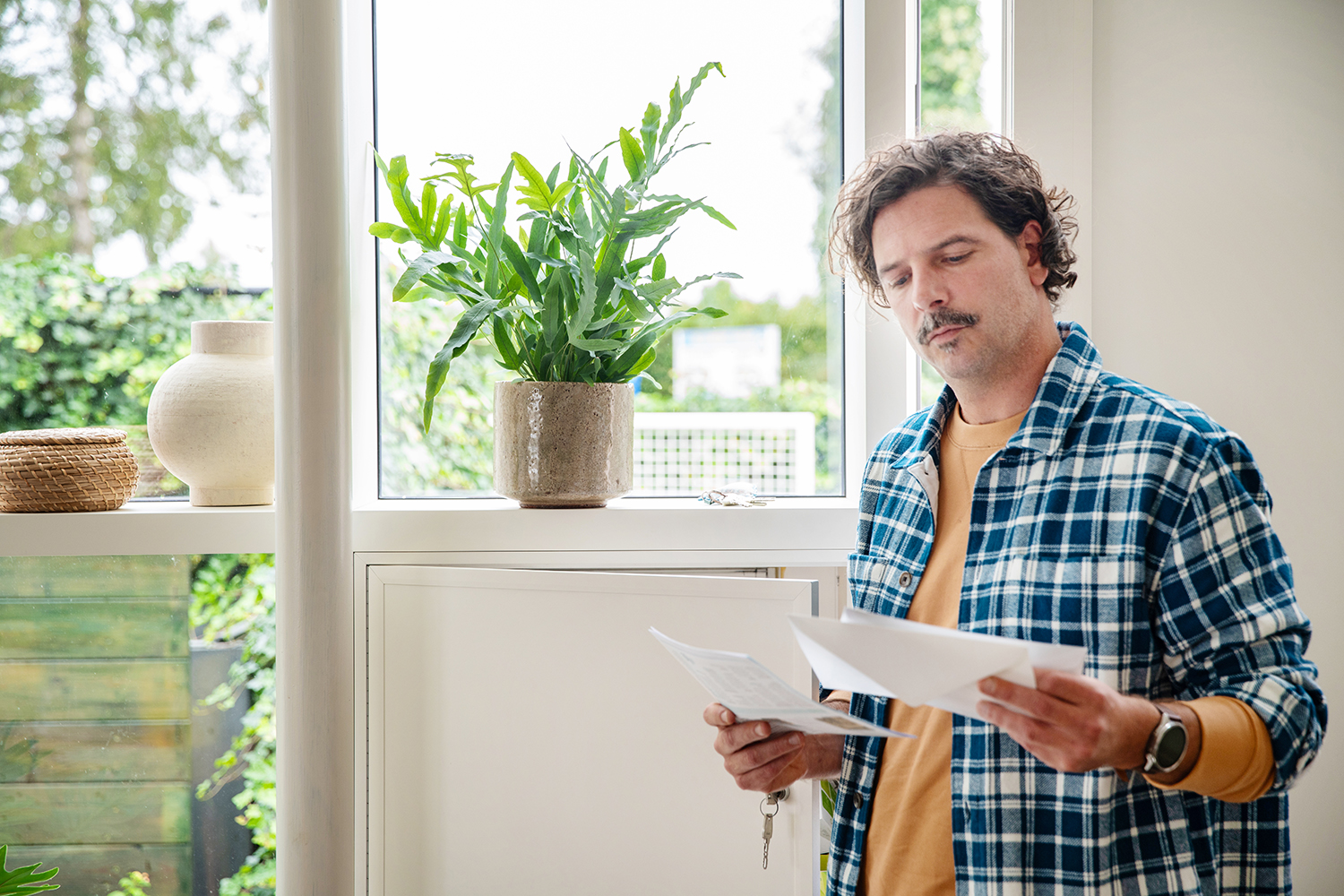 Blauwvaren in indirect licht naast een venster, een man haalt zijn post op in de voorgrond - Aveve