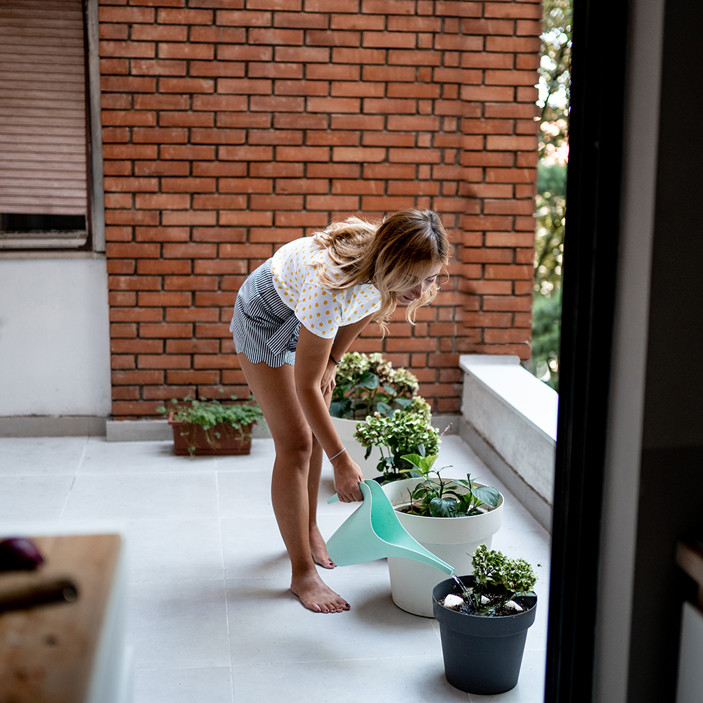 Afbeelding van een vrouw die planten water geeft op een terras