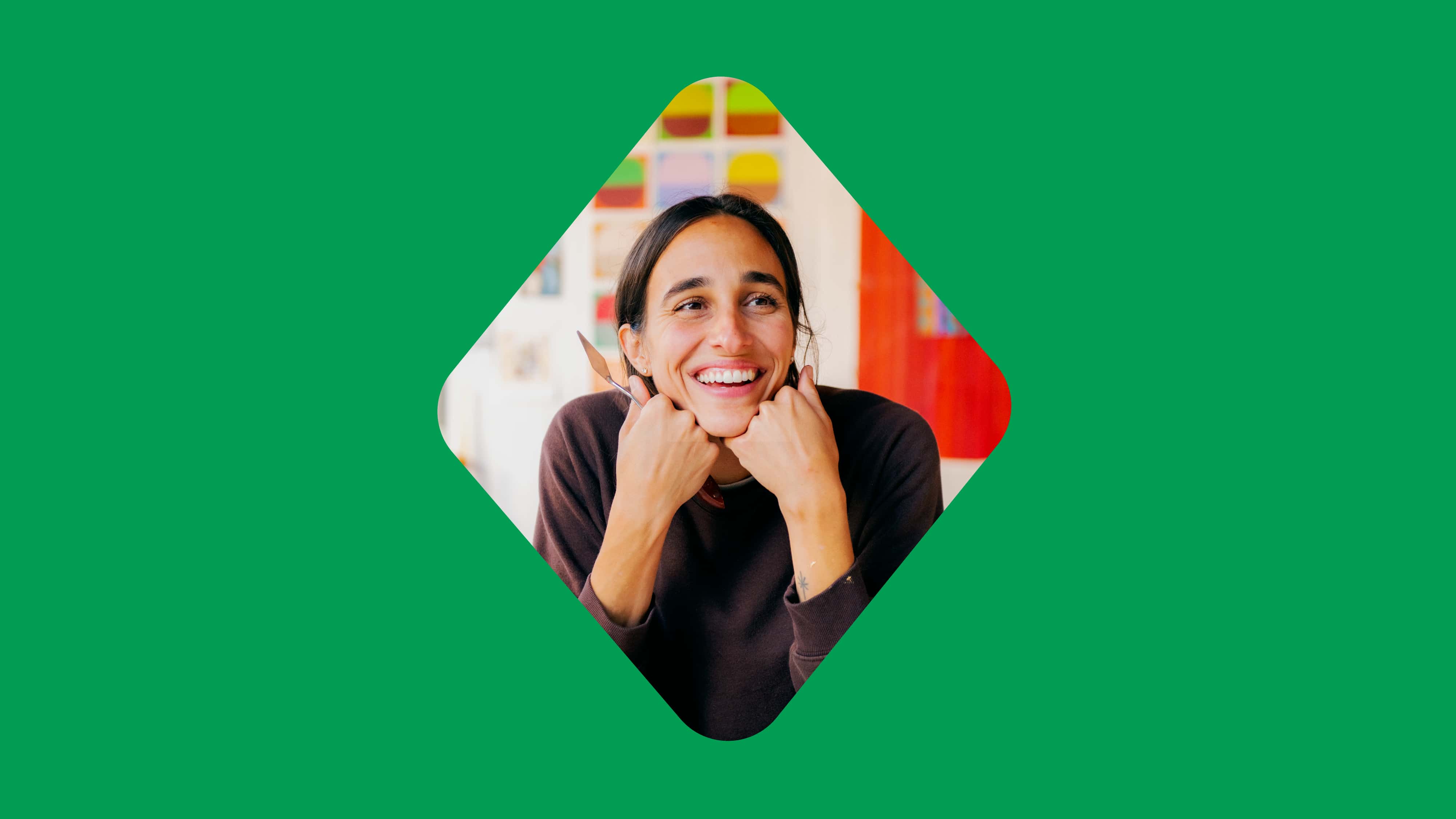 A smiling woman rests her chin on her hands inside a diamond cutout against a green background.