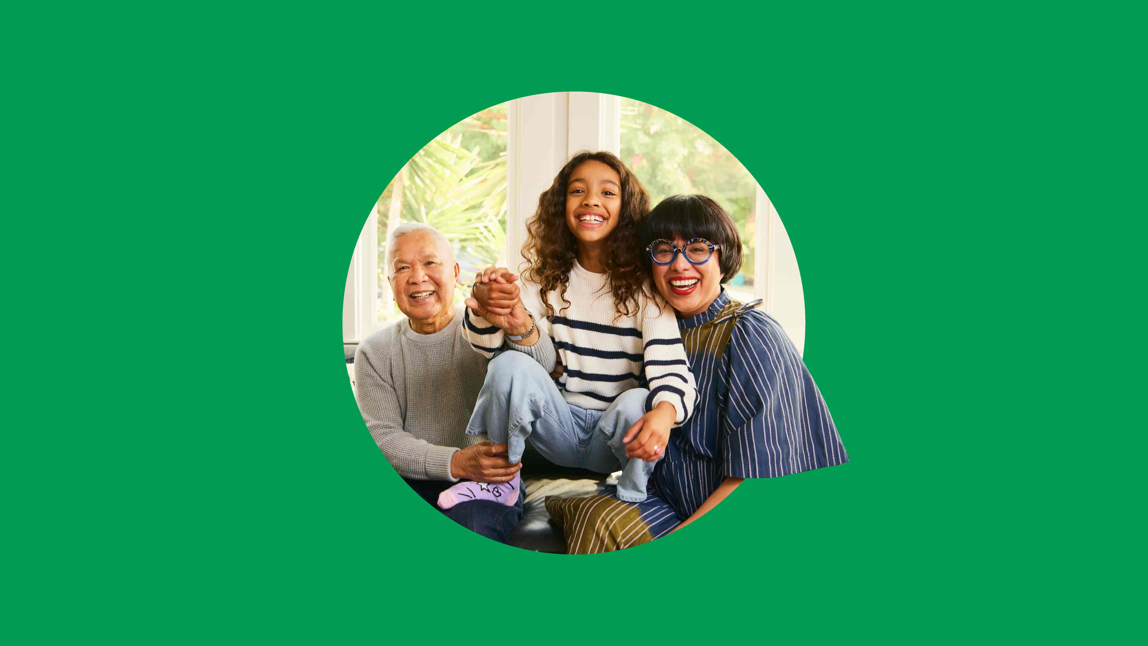 A family of three sitting together on a couch, with a vibrant green background behind them.