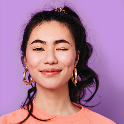 A model with dark thick wavy hair in a peach shirt. | Waterless Hair Care