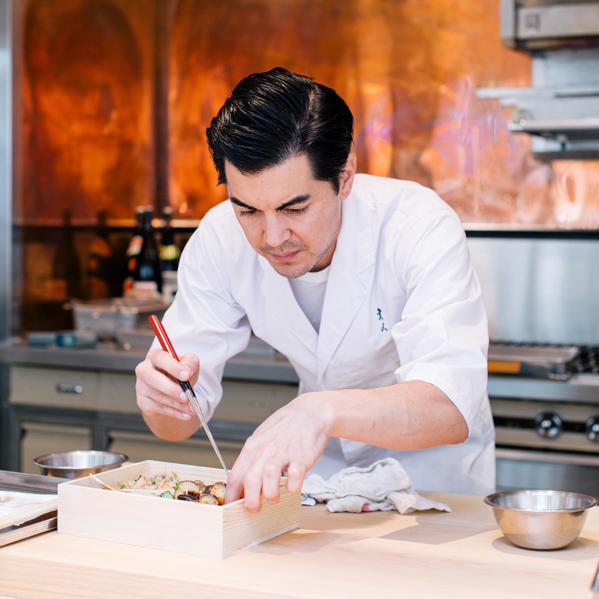 chef plating a box with japanese food in kitchen