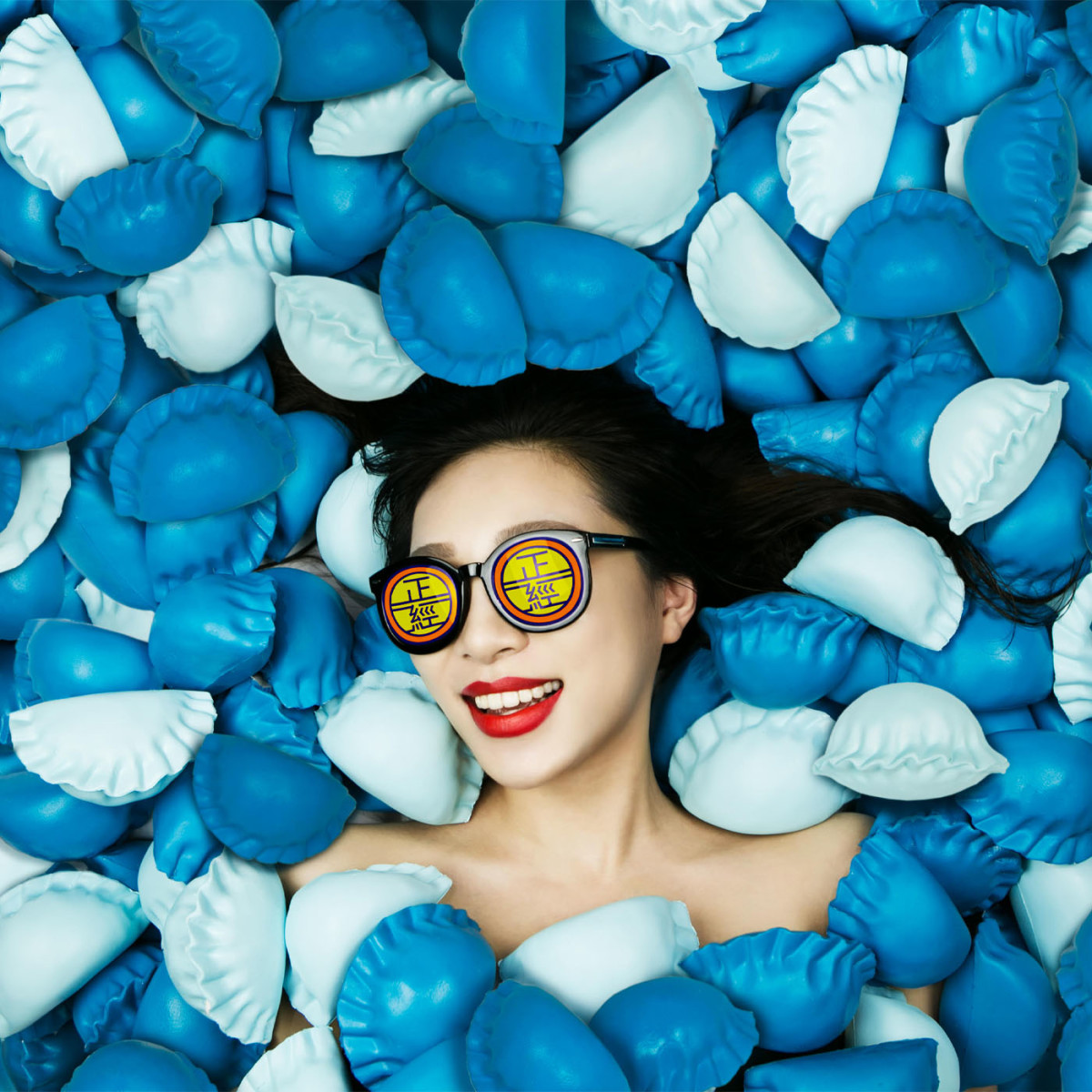 Woman wearing text-on-lens sunglasses while lying in a sea of blue dumplings
