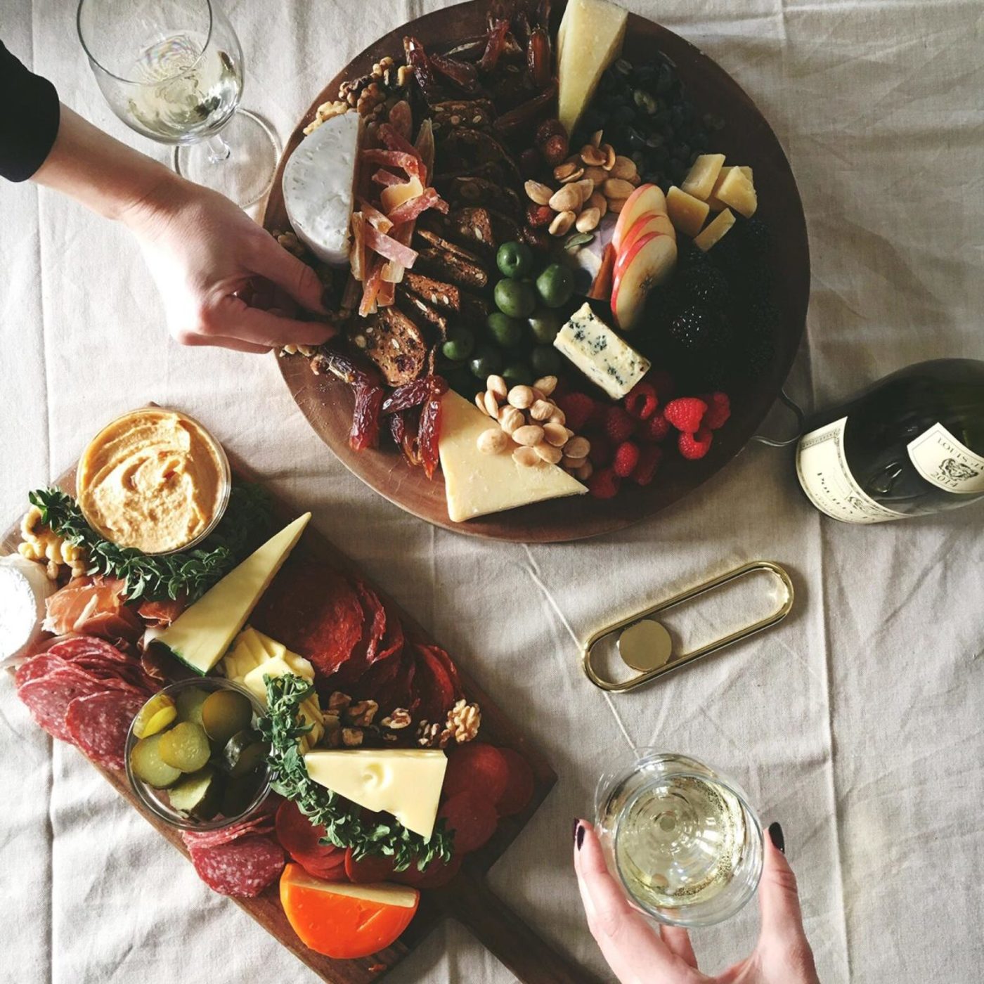 flat lay of charcuterie and cheese plate with wine glasses and bottles and a bottle opener