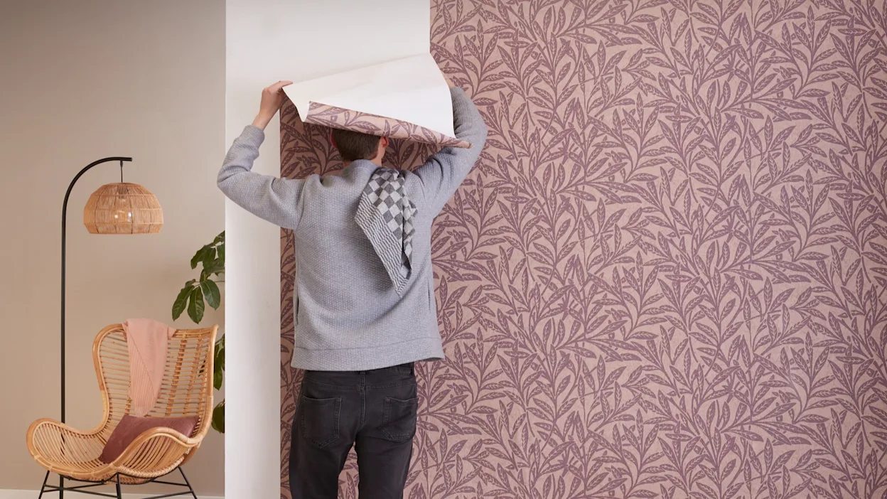 Sfeersetting waarbij een man behang op de muur plakt