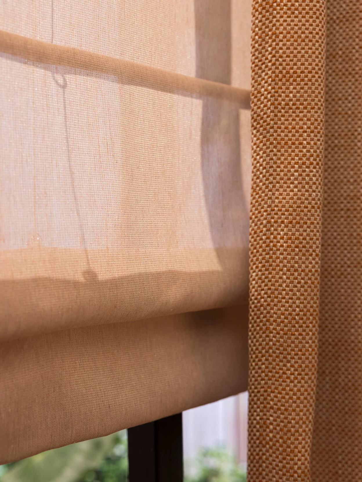 Close-up van een terra gordijnstof met een subtiel werkje en een lichtroze inbetween vouwgordijn