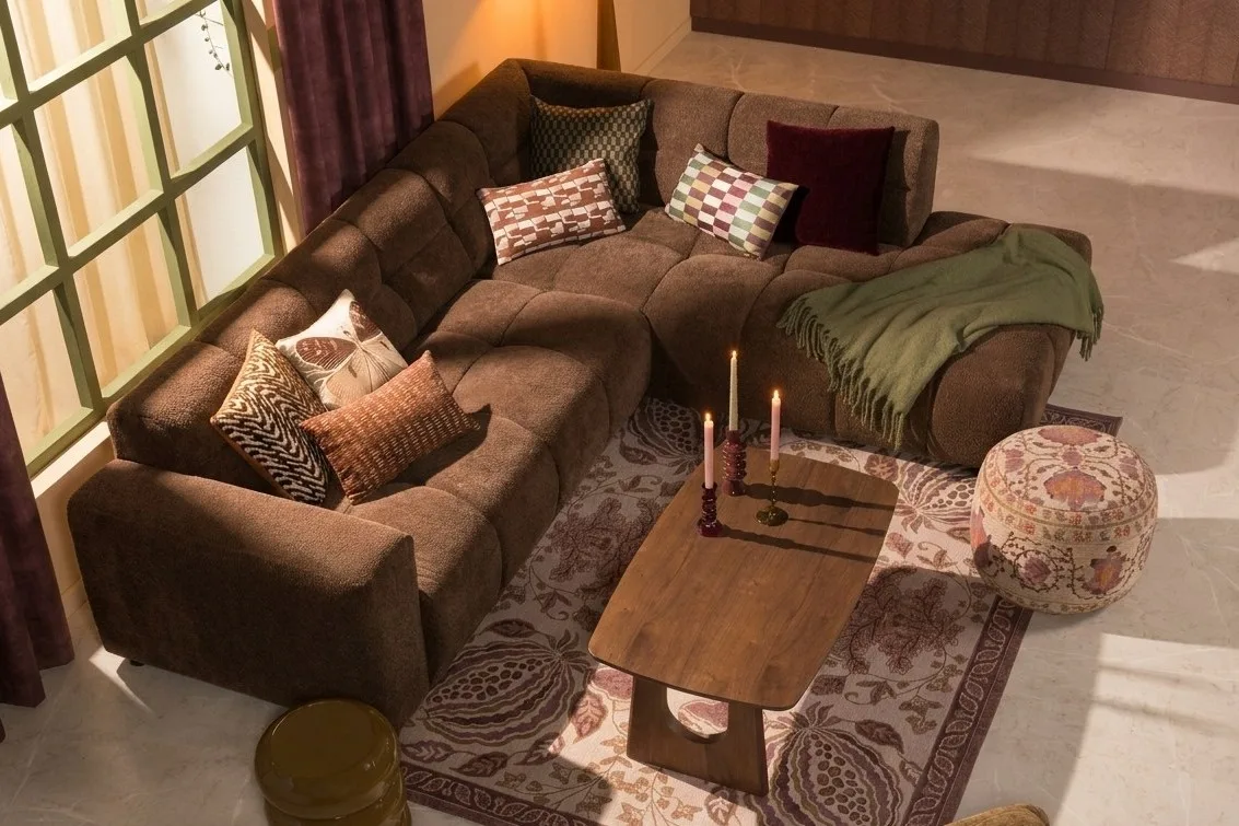 Bohemian woonkamer met een bruine bank, vloerkleed en poefje met boho print en sierkussens.
