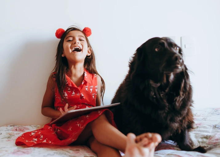 Image of a young girl sitting next to a dog and laughing