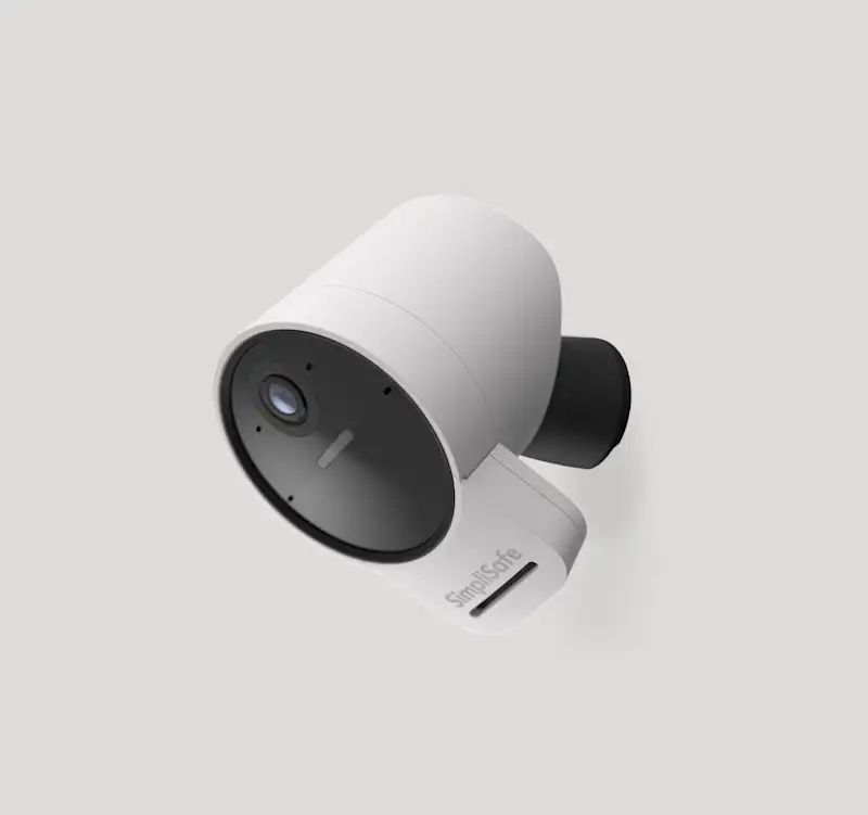 SimpliSafe Outdoor Camera with spotlight illuminated against a dark background. Heading reads: 'Outdoor Camera.' Body text reads: 'Stop potential intruders in their tracks with a bright spotlight. Agents see and speak to intruders with select monitoring plans.' Badge reads: 'Runs on rechargeable battery or included power cable.'