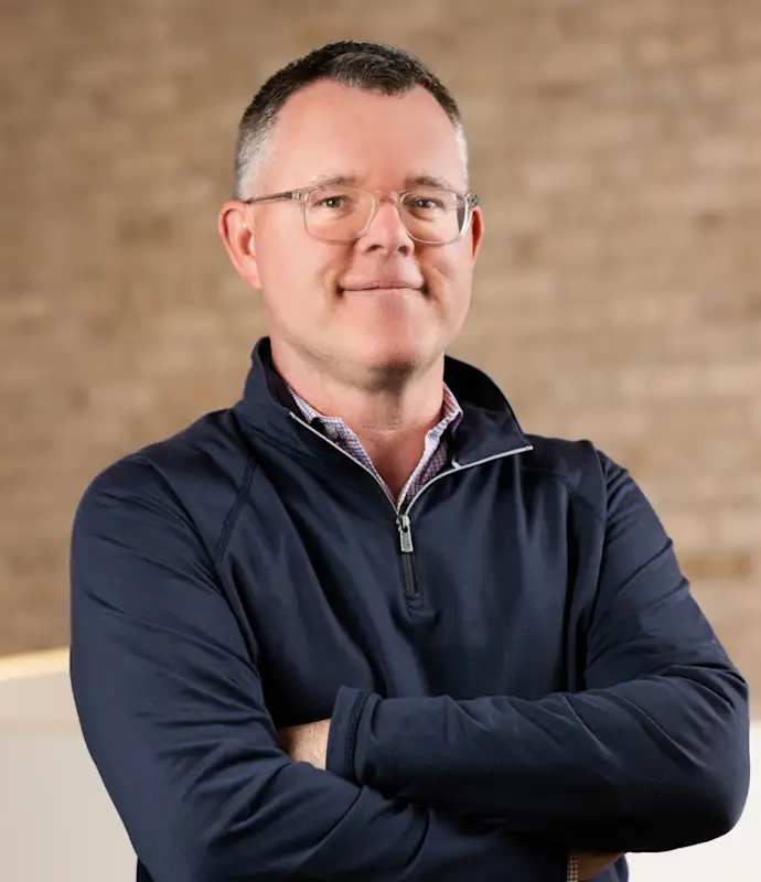 Mark FitzPatrick standing with arms crossed in an indoor setting.