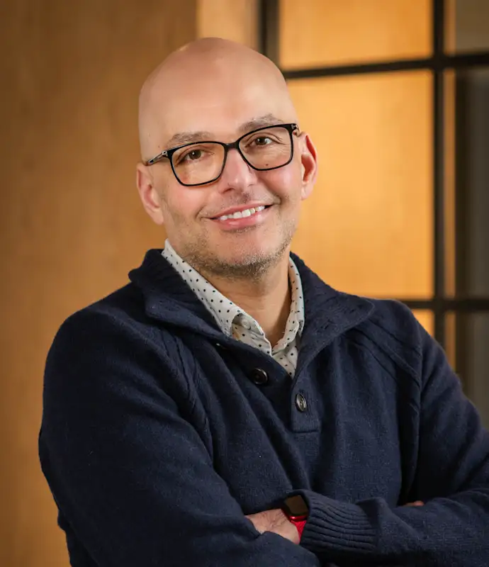 Hooman Shahidi smiling and standing with arms crossed in an indoor setting.