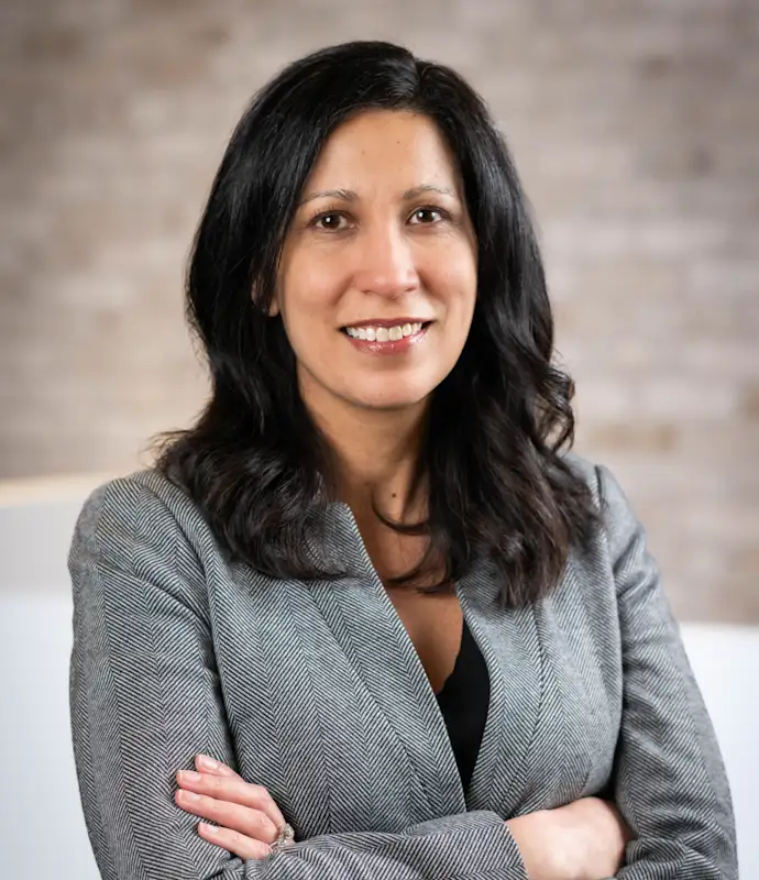 Vanessa Karlis smiling and standing with arms crossed in an indoor setting.