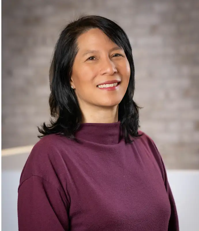 Ai-Li Lim smiling in front of a brick wall background.