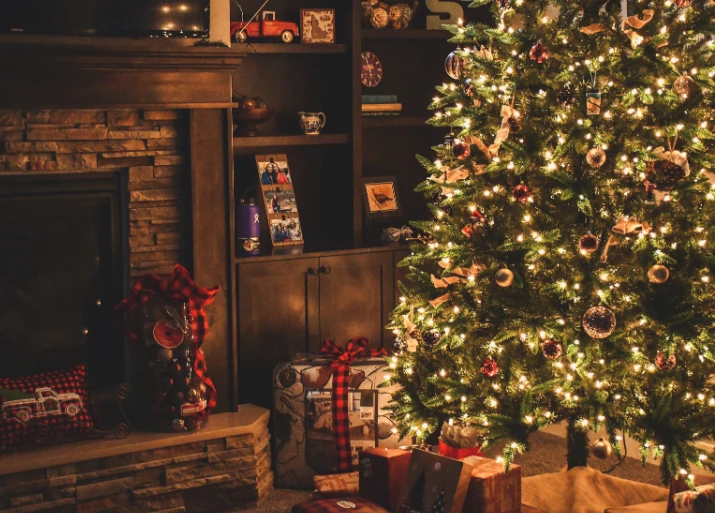 Image of a living room with a Christmas tree in front of a fireplace, lights, and gifts under the tree