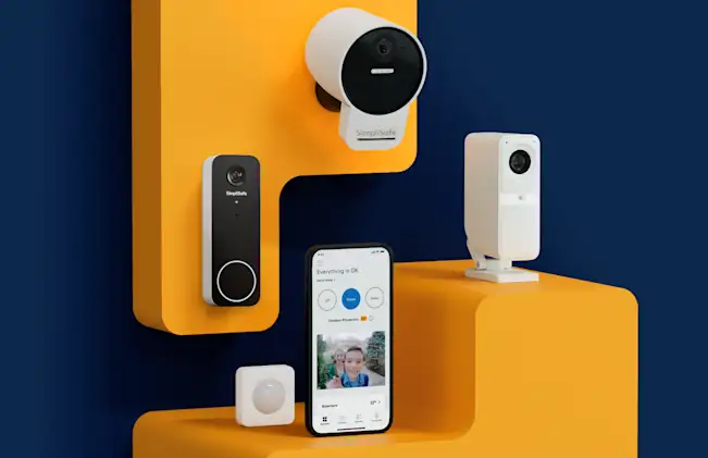 A SimpliSafe Indoor Camera, Outdoor Camera, Video Doorbell, and Motion Sensor arranged around a smartphone that is displaying the SimpliSafe app.