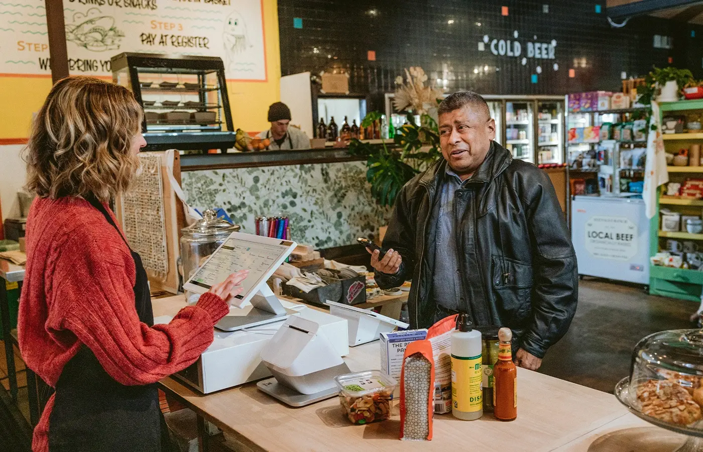 Cashier ringing up a customer's items using a Station Duo. Customer is holding a phone, waiting to use tap to pay on Mini.