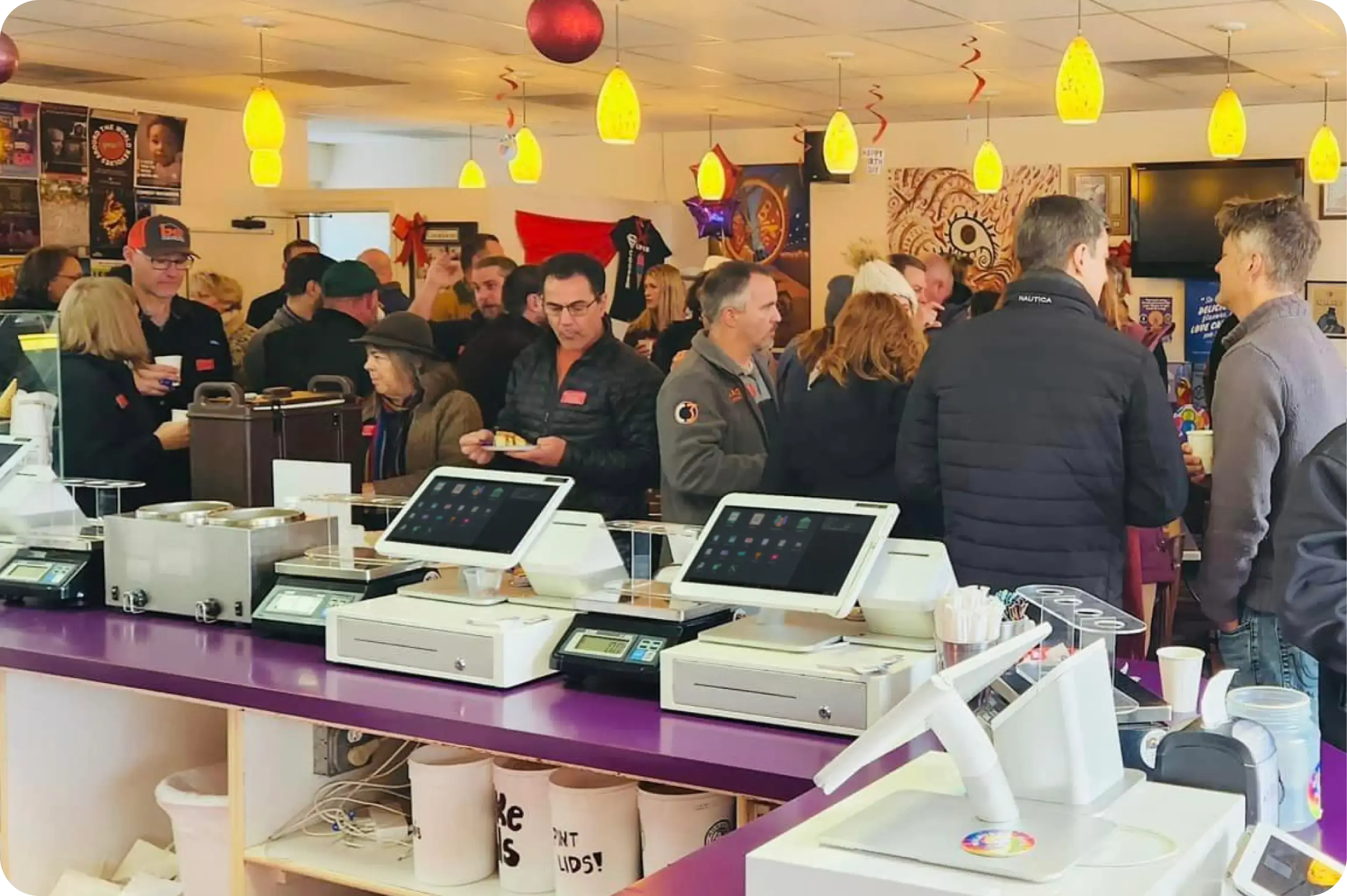 Dozens of customers socializing at an ice cream shop event. At checkout, there are four Station Duos sitting on cash boxes and weight scales with ice cream holders.