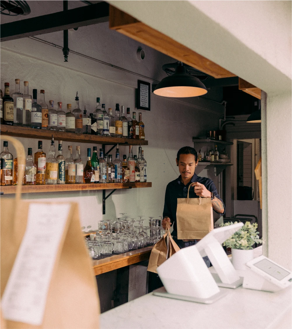 Restaurant worker behind a bar carrying prepared takeout orders to the register for pickup