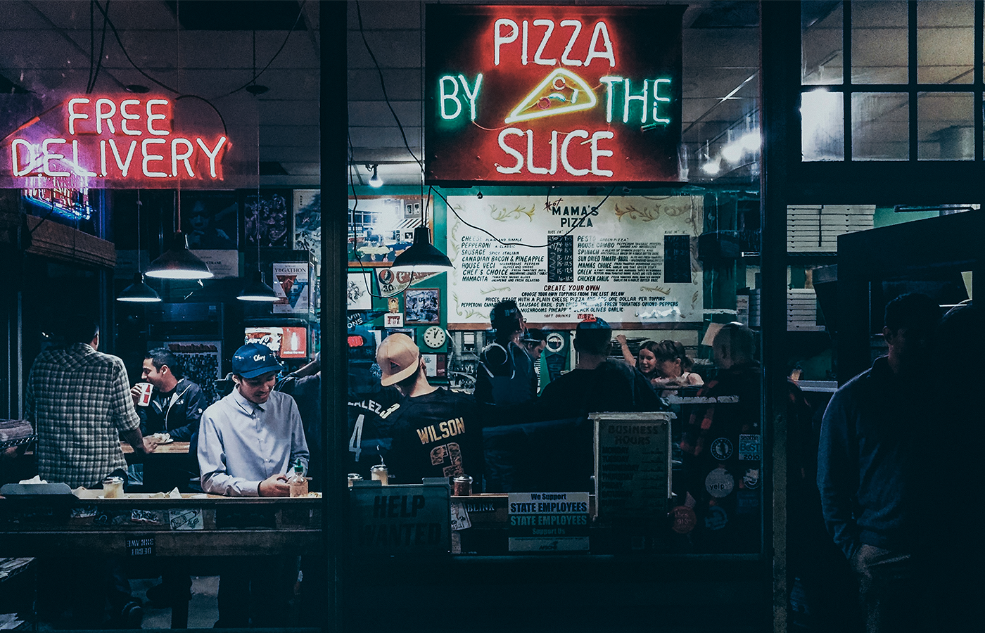 Pizzeria storefront with signs that read "free delivery" and "pizza by the slice"