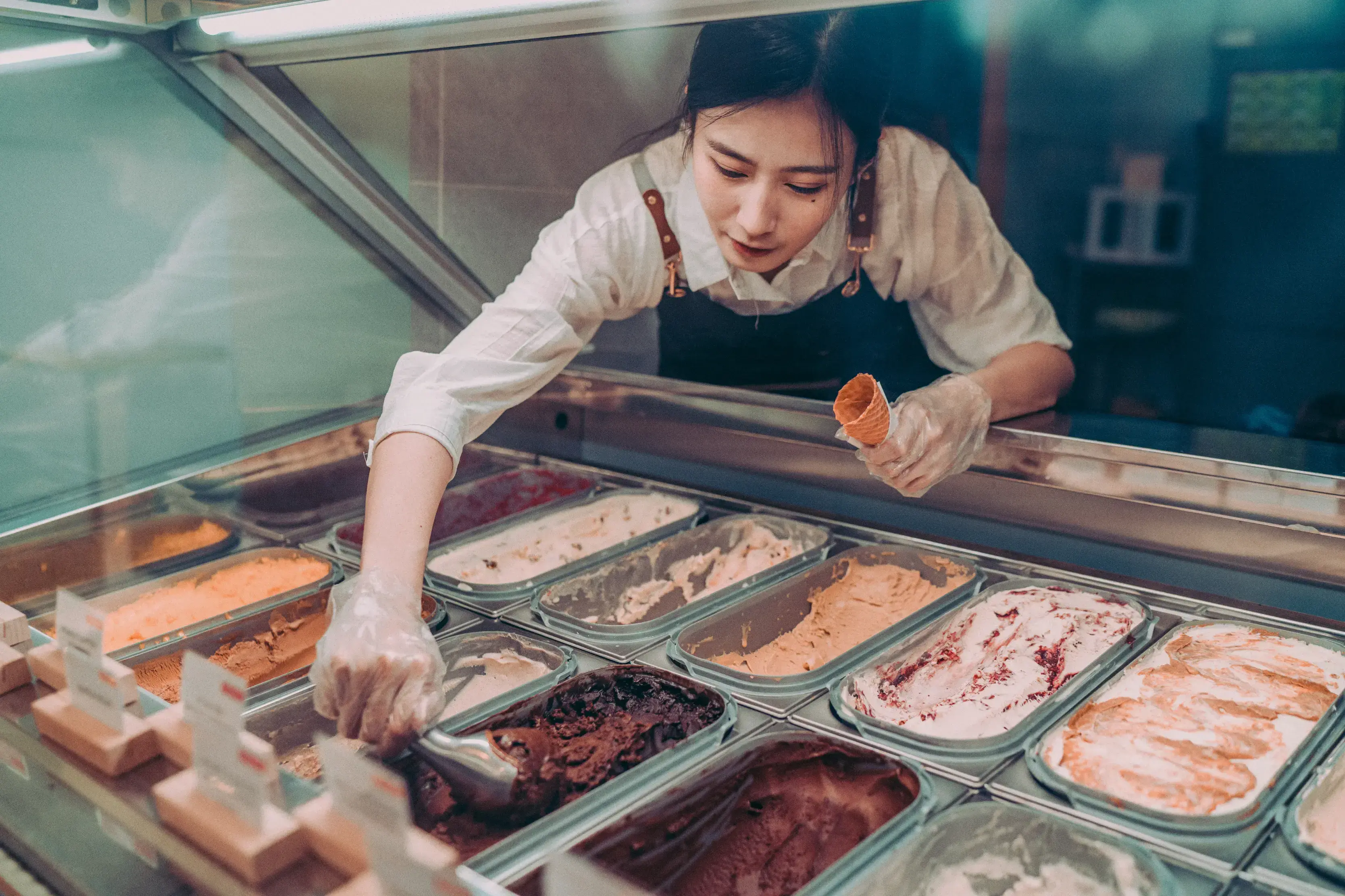 Ice cream store attendant scoops ice cream while holding a cone