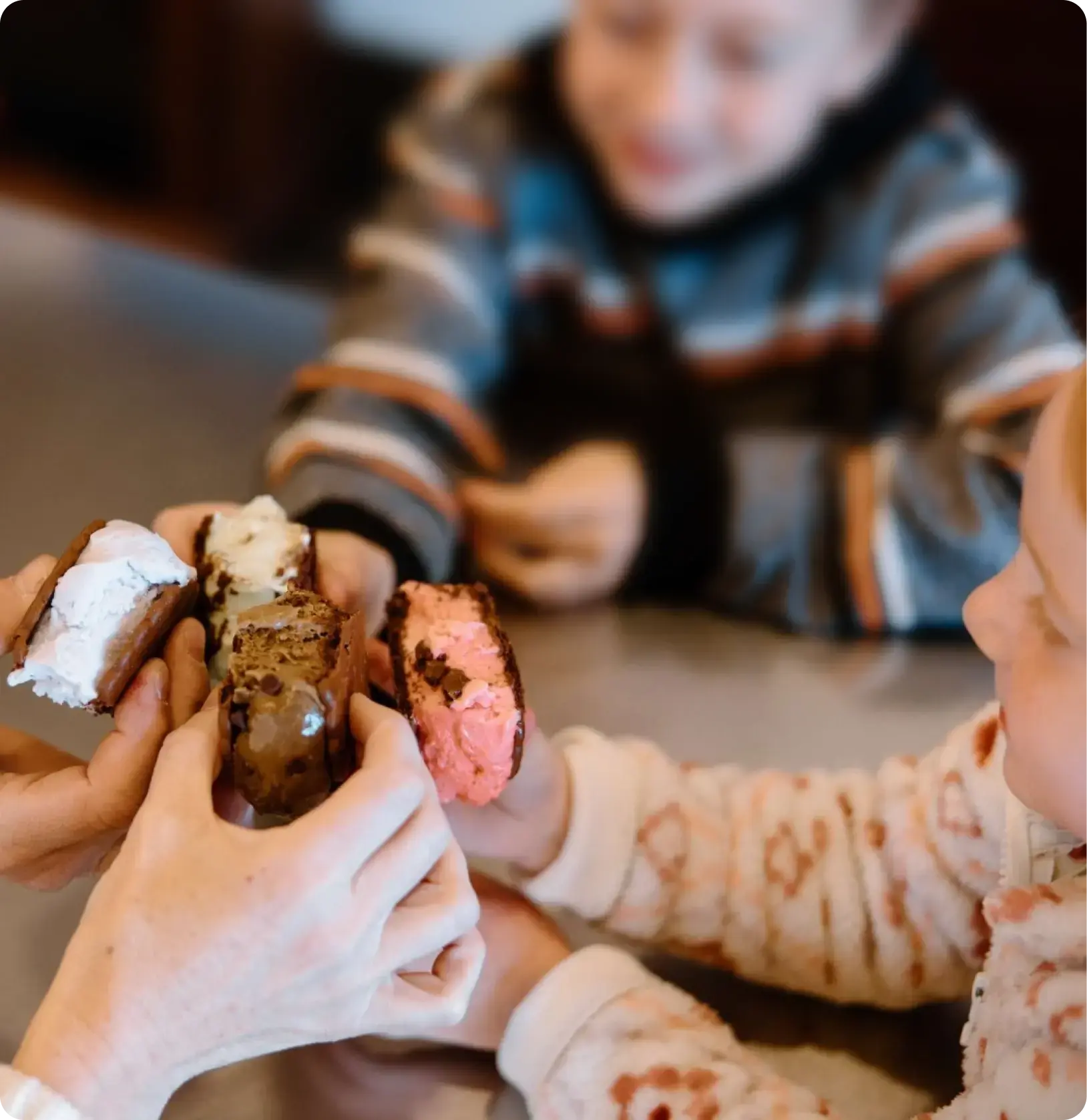 Two adults and two children sitting at a table holding ice cream sandwiches out into the center of the table.