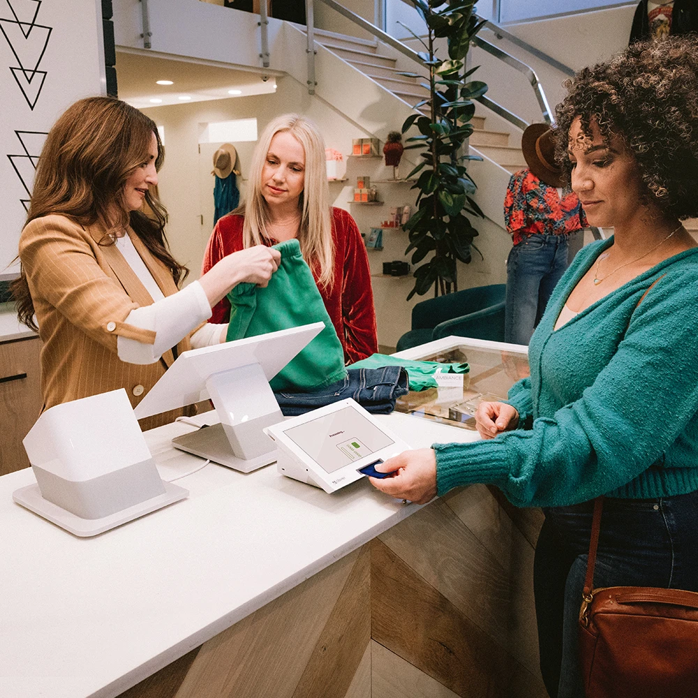 Customer pays for clothes by inserting credit card into reader while cashier folds purchased clothes.