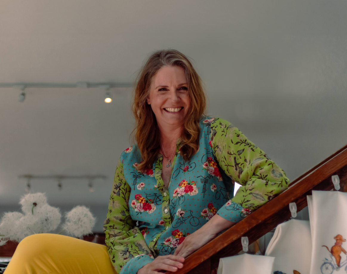 Woman standing on a staircase leaning onto the rail while wearing a colorful shirt and bright pants.