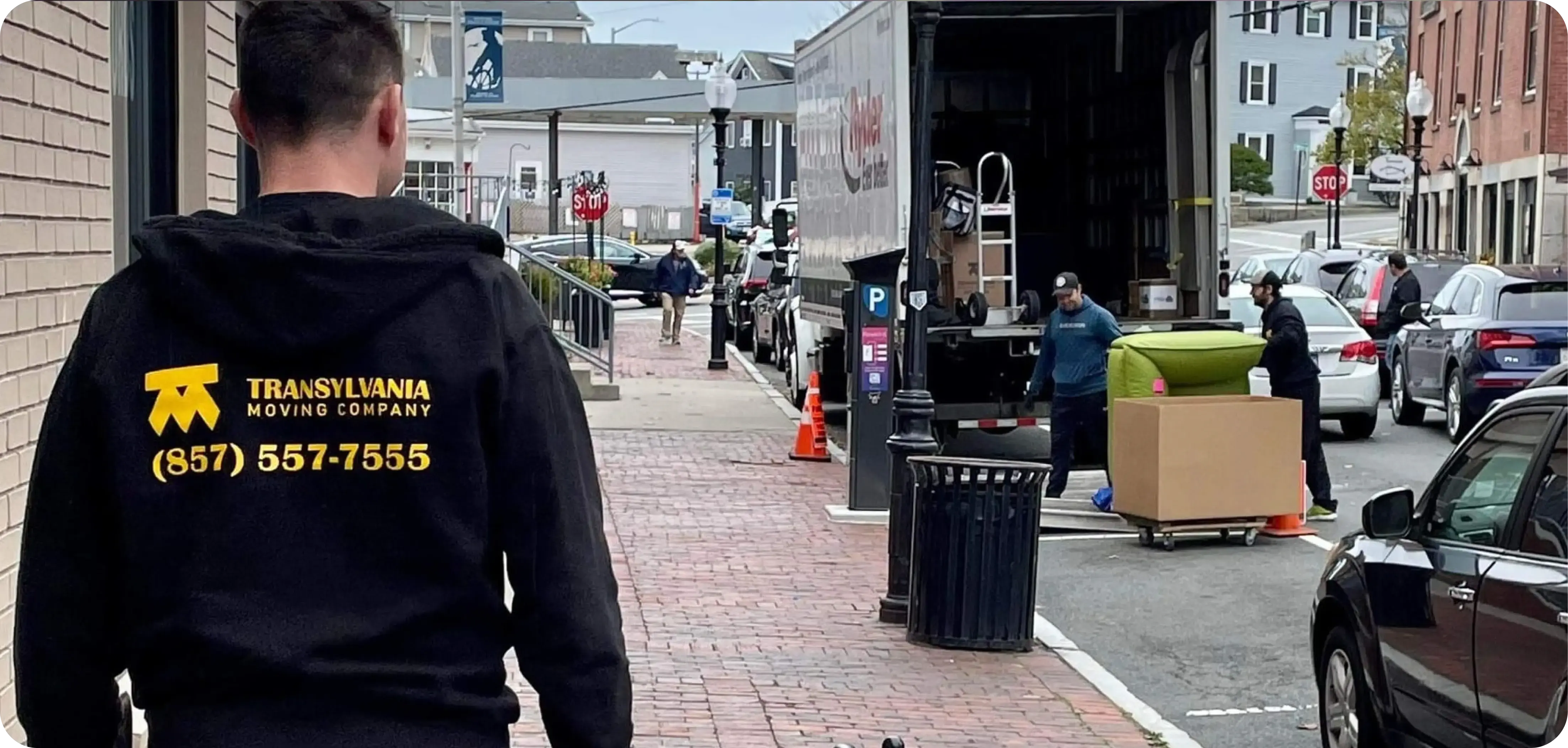 Transylvania moving company employee walking on a sidewalk toward a crew of movers handling furniture 