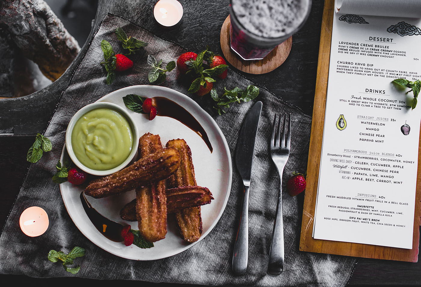 Churros with avocado mousse and raspberries served on dark napkin; mint garnish, candles, and dessert menu create cozy vibe.