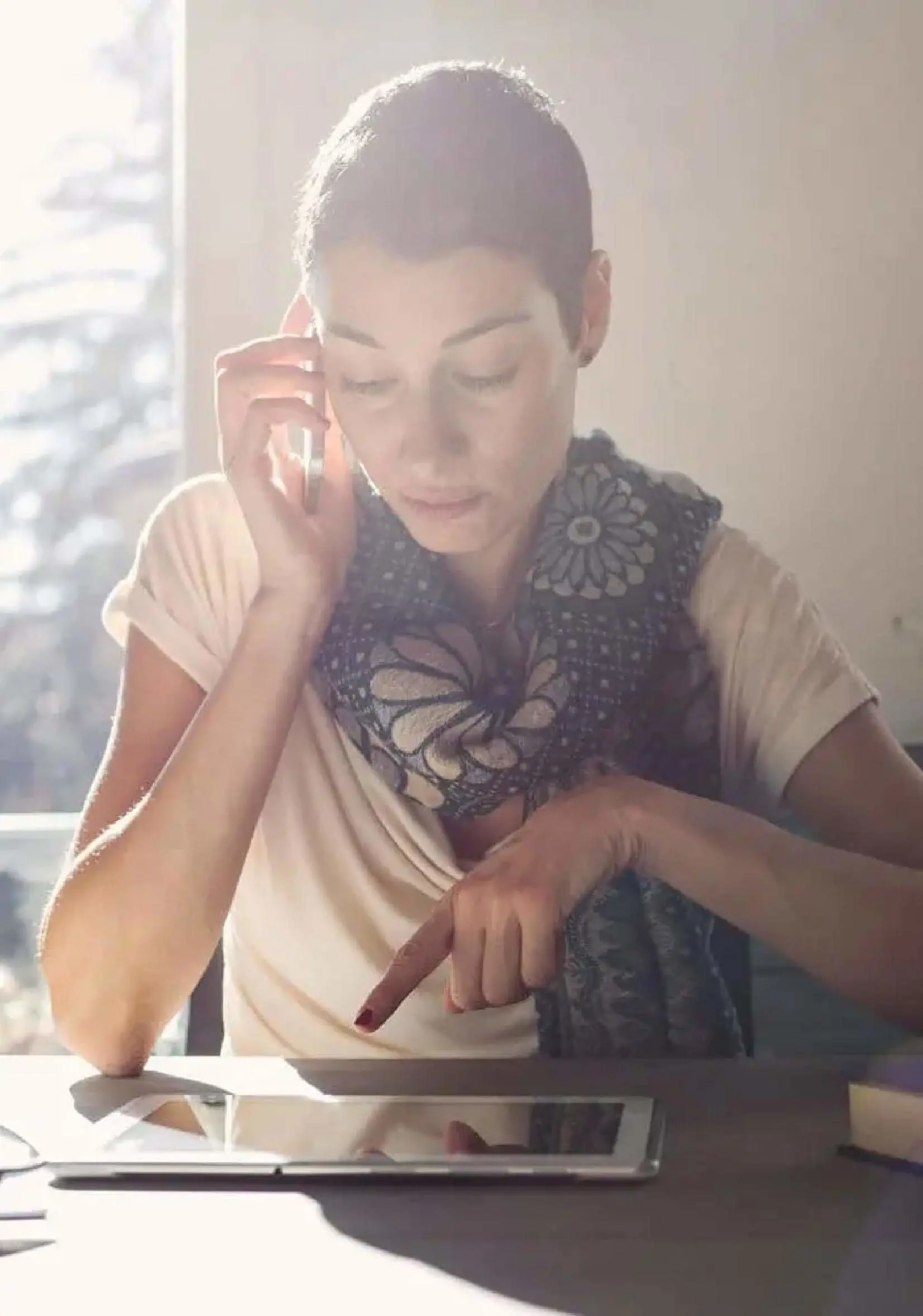 A woman is looking into a tablet and talking on mobile