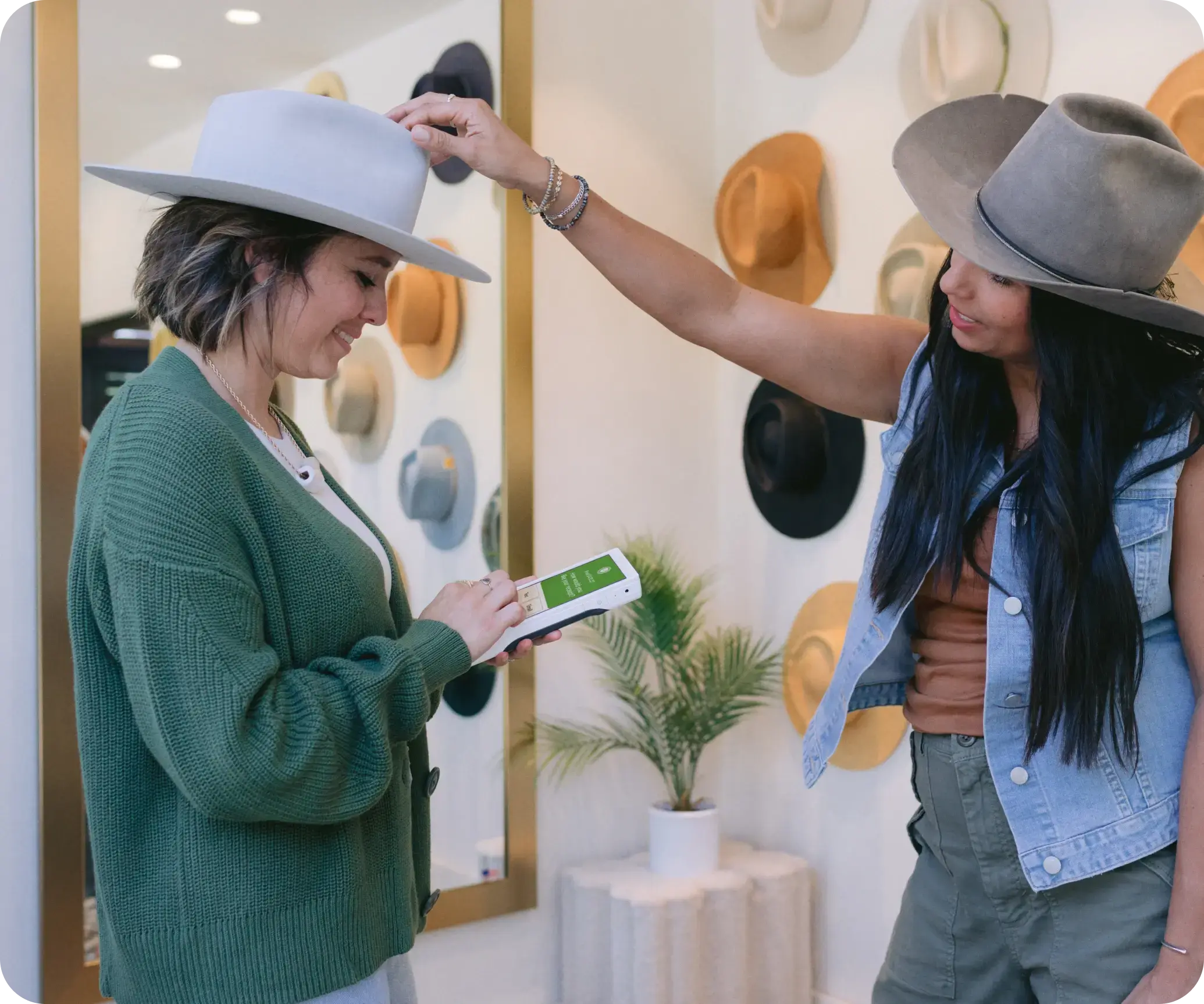 Woman standing in a boutique hat shop paying for her custom hat, while the shop owner places the hat on the customer's head.