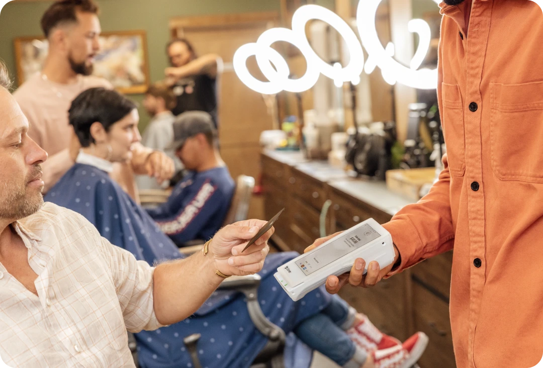 Man in salon paying for his haircut by tapping his credit card on a Flex device while the barber holds the device.