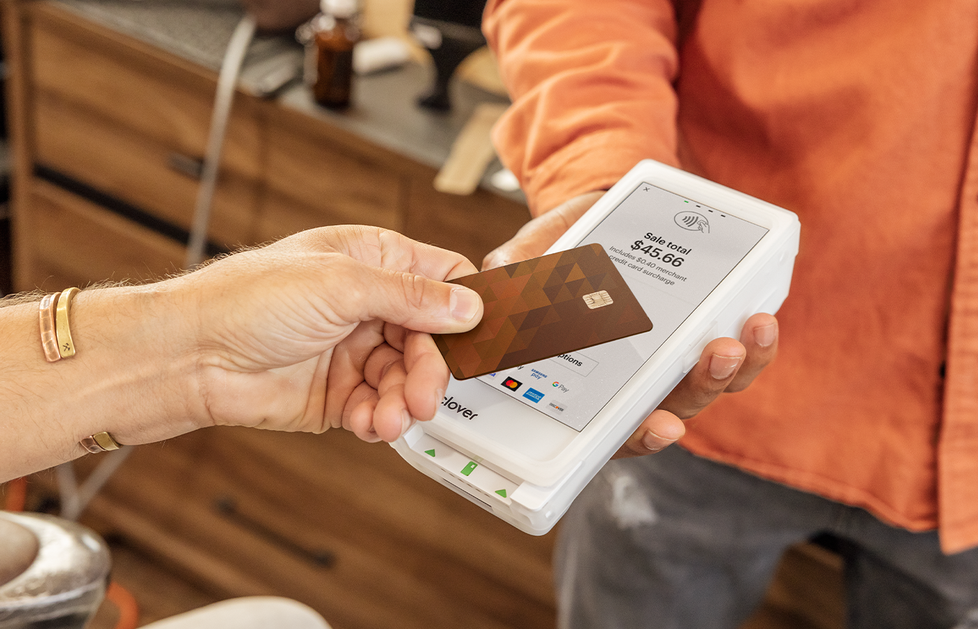 Hand holding credit card above Clover Flex, held by merchant, performing a contactless payment. 
