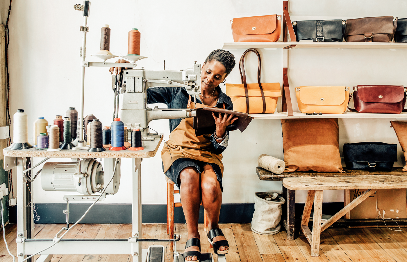 Image of a woman using a sewing machine to create leather bags.