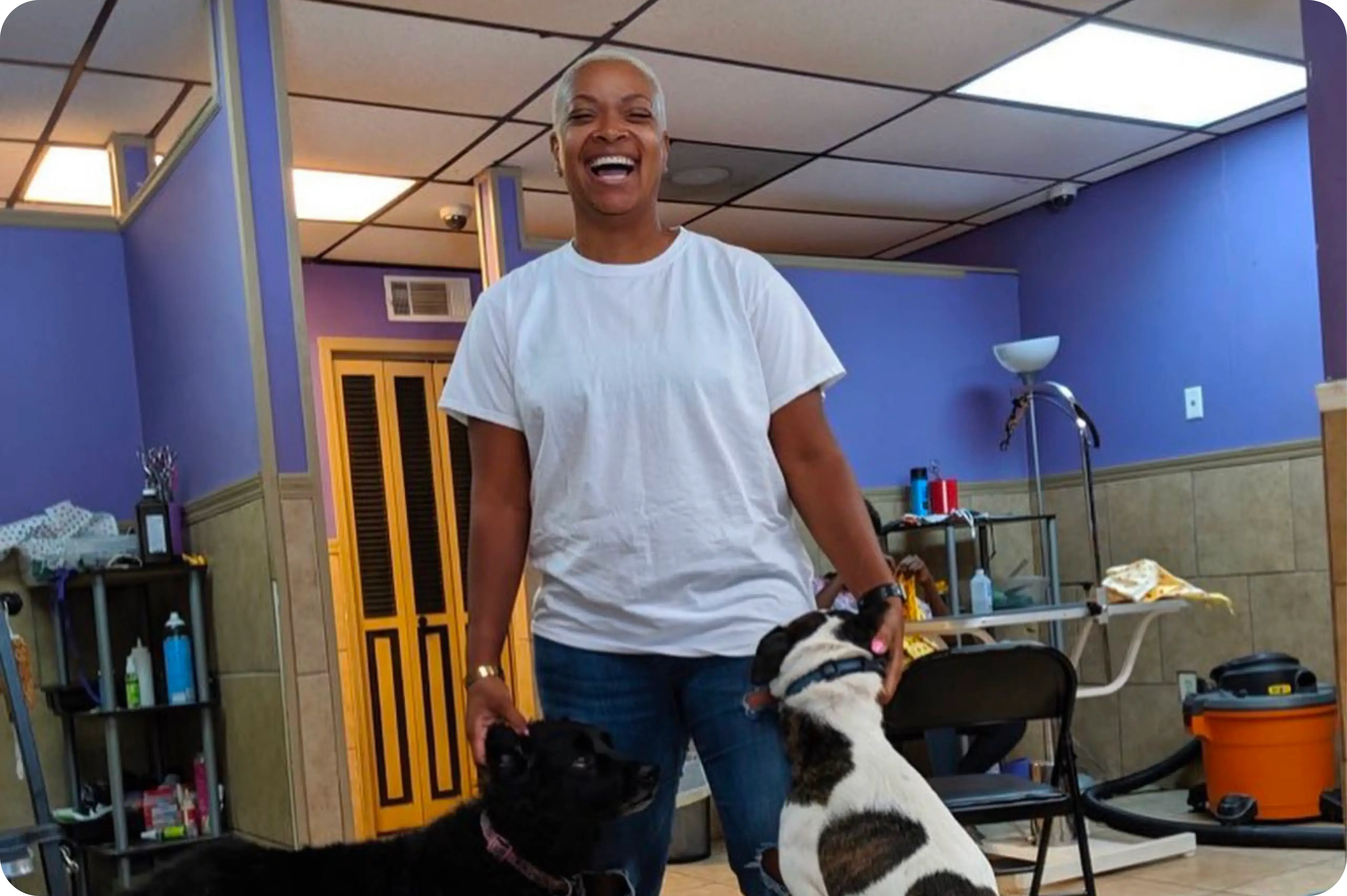 Owner of chateau 4 paws standing in their grooming shop smiling while petting two dogs