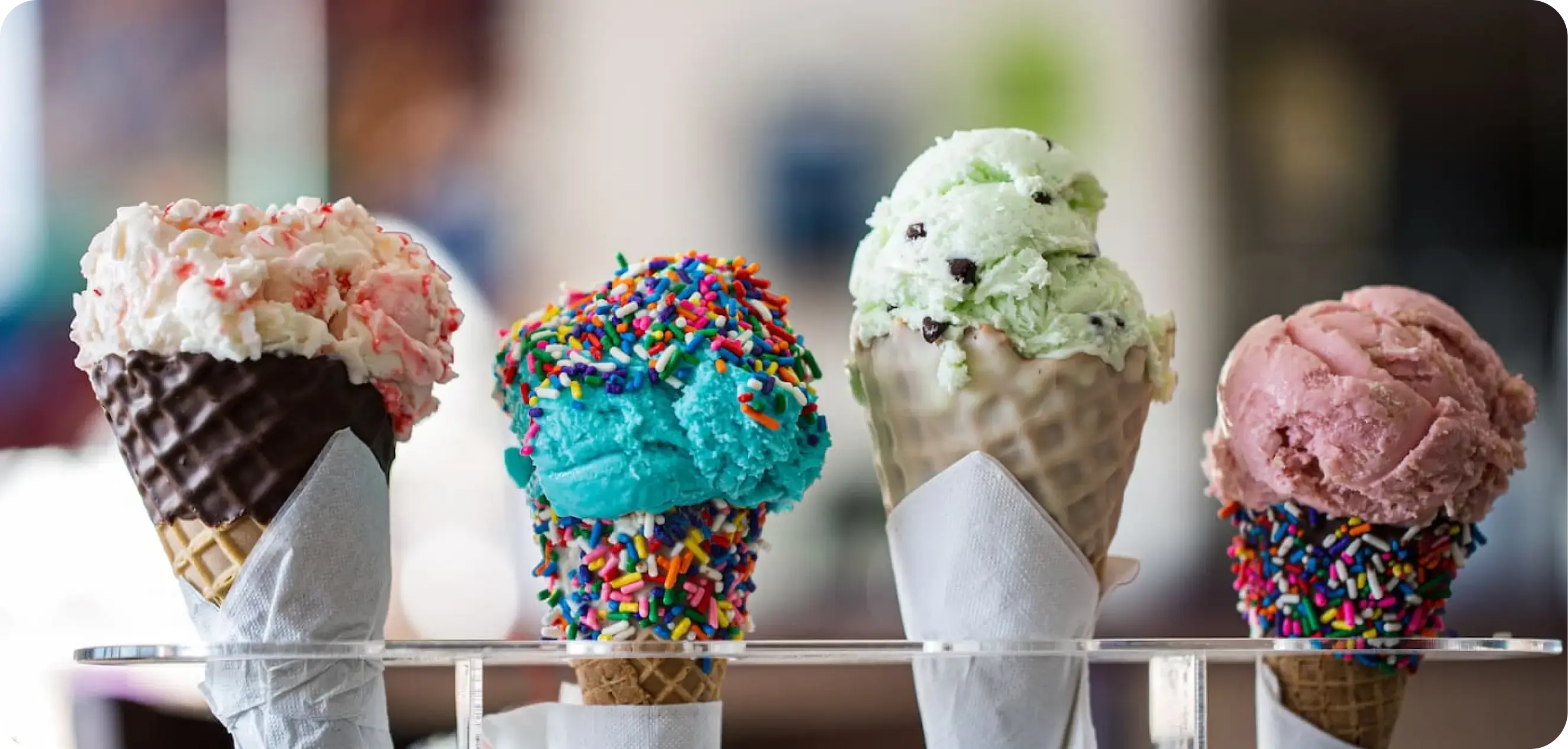 Four chocolate-dipped ice cream cones with different ice cream flavors in them lined up in a cone holder.