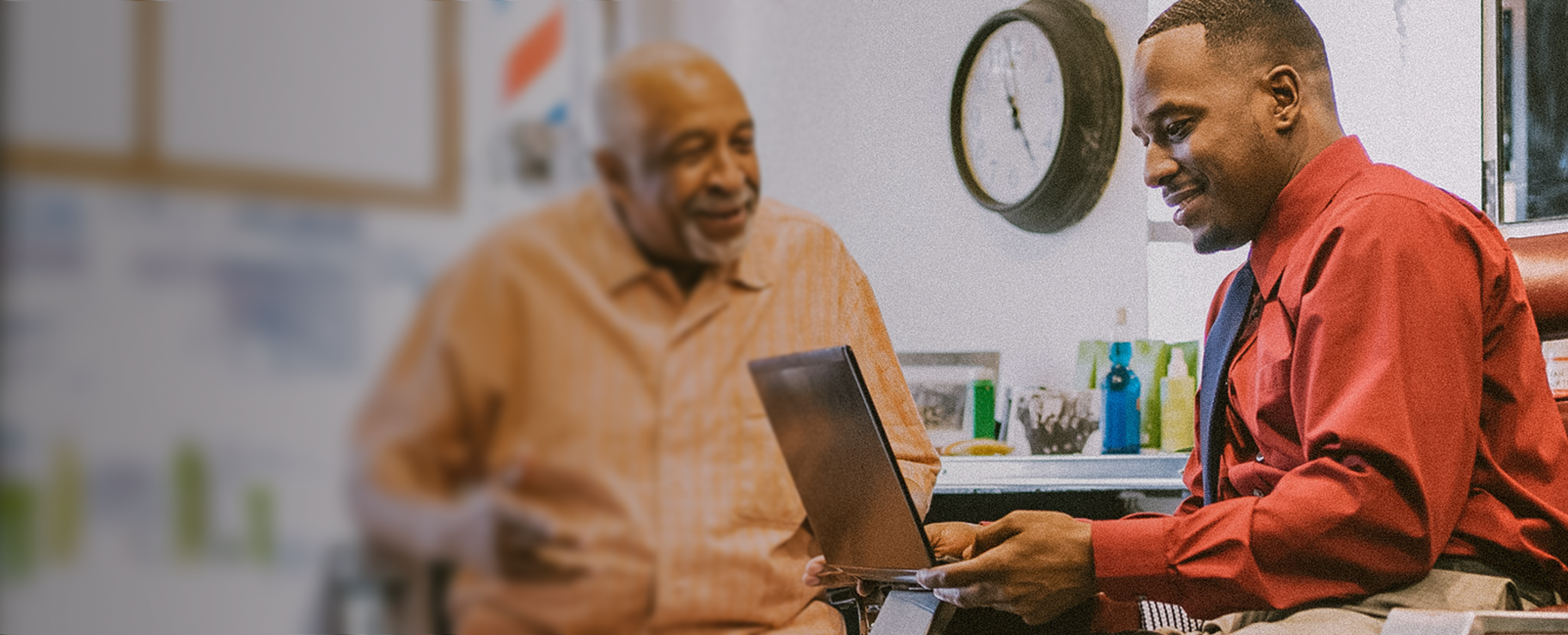 An old man discussing something with a professional who is holding an open laptop.