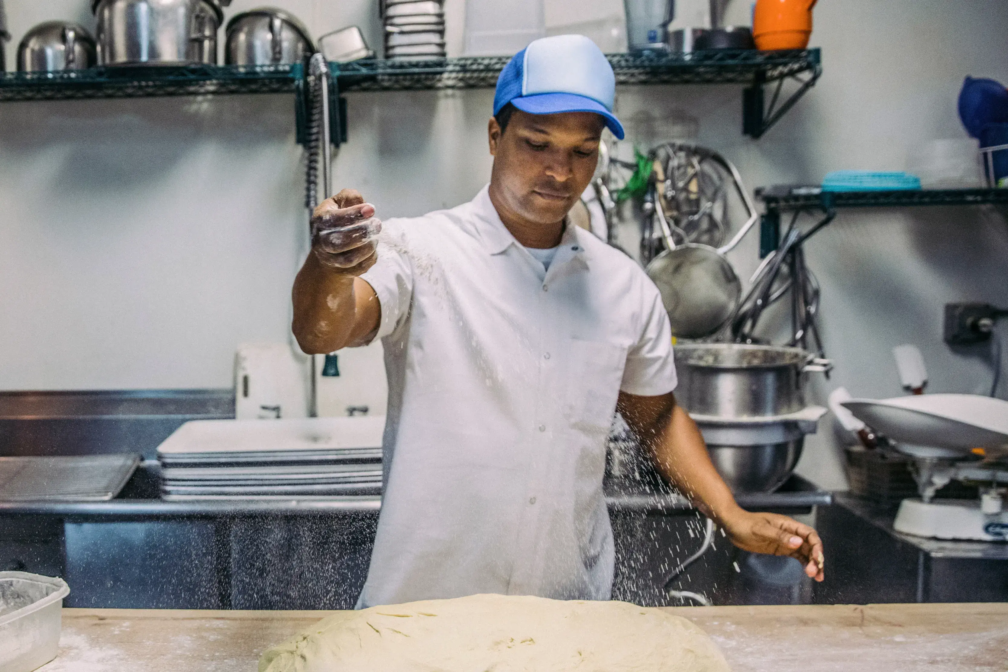 Baker sprinkles flour over dough