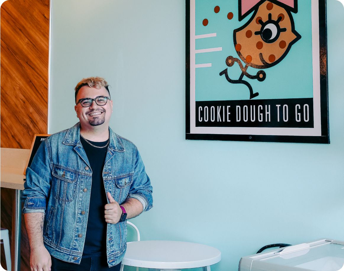 Store owner posing in front of a blue wall in their store that has their company logo on it