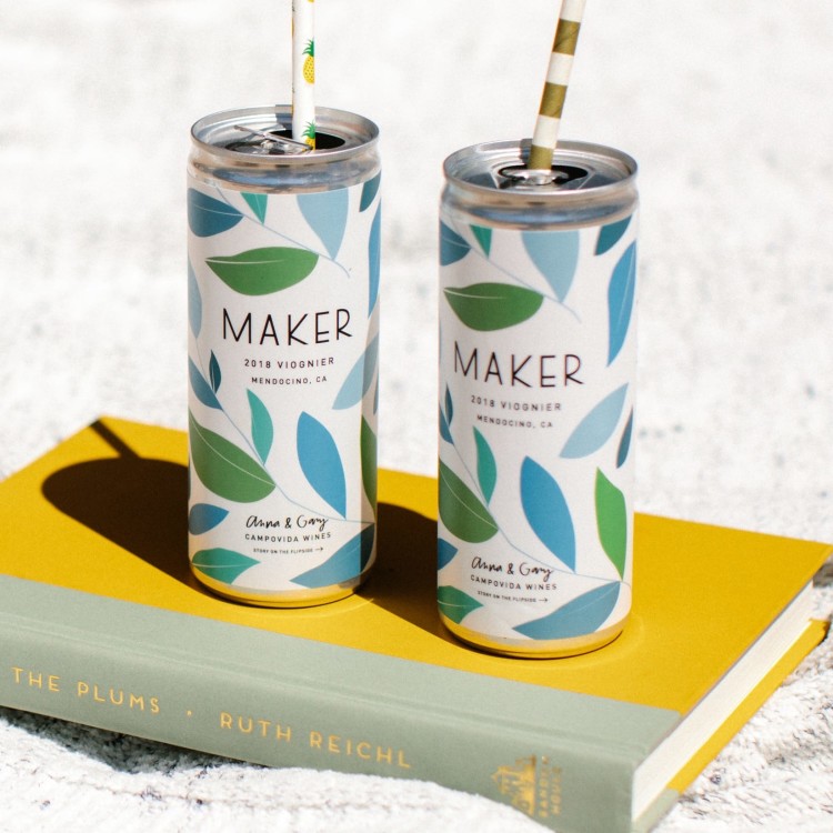 2 cans of 2019 Viognier on book on sand with straws