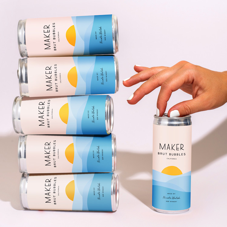 united airlines and maker wine brut bubbles cans stacked on top of one another on the left, with a hand opening a can on the right