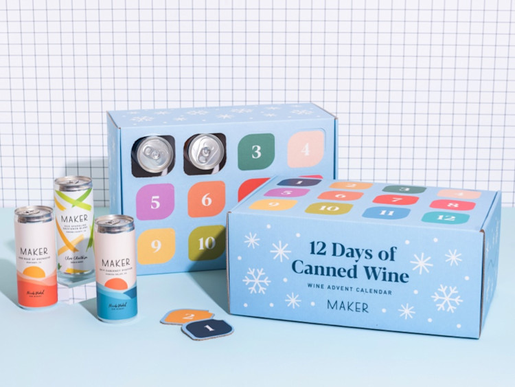 Two advent calendar boxes. The first shows the twelve days that can be opened to reveal cans of wine, while the other shows the "12 Days of Canned Wine" title. Three cans of wine sit next to the boxes.