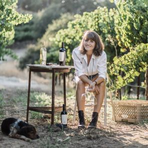 Alice Sutro sitting with a bottle of wine in her vineyard